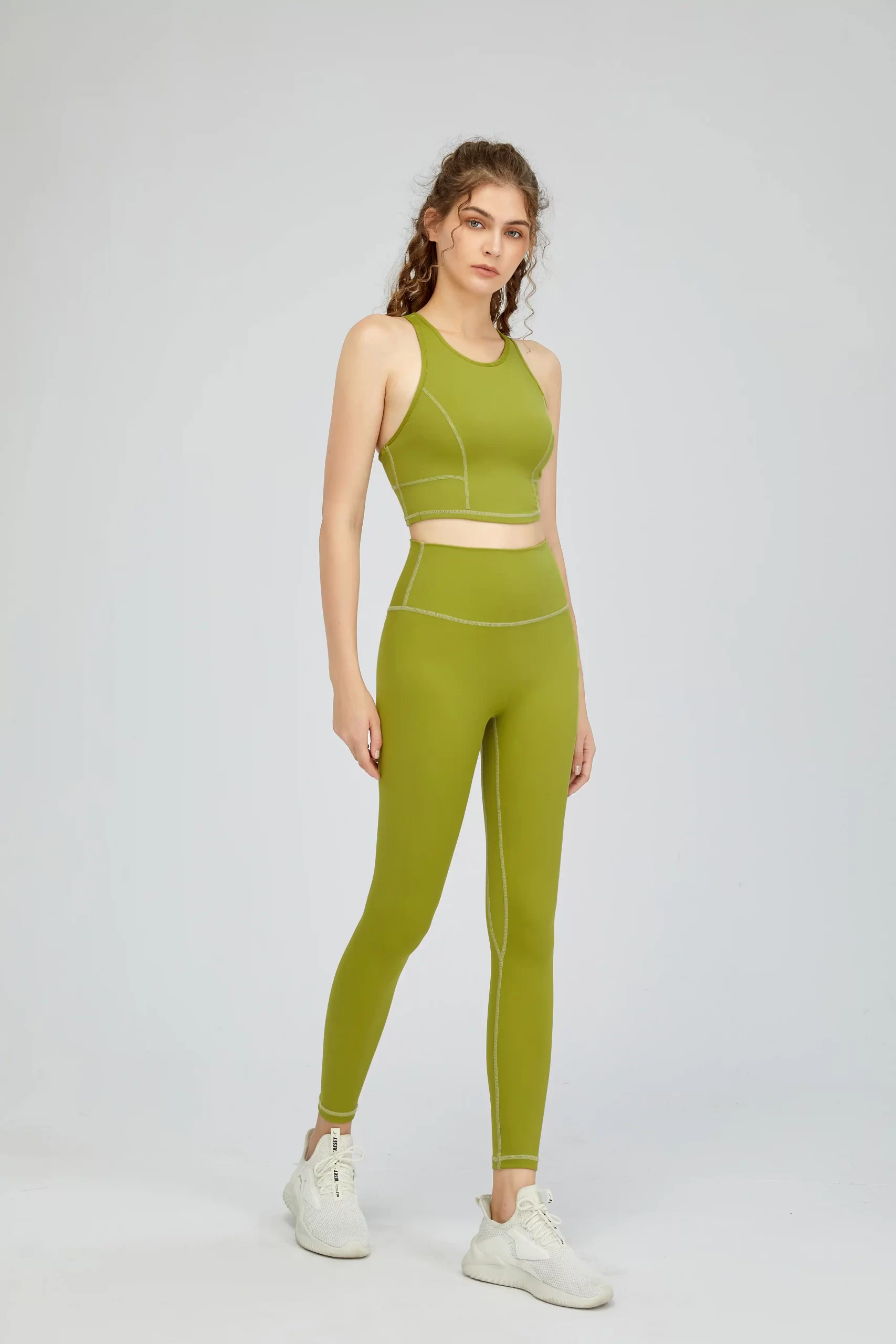 Model wearing green high-waisted leggings and sports bra, standing in full body front pose.