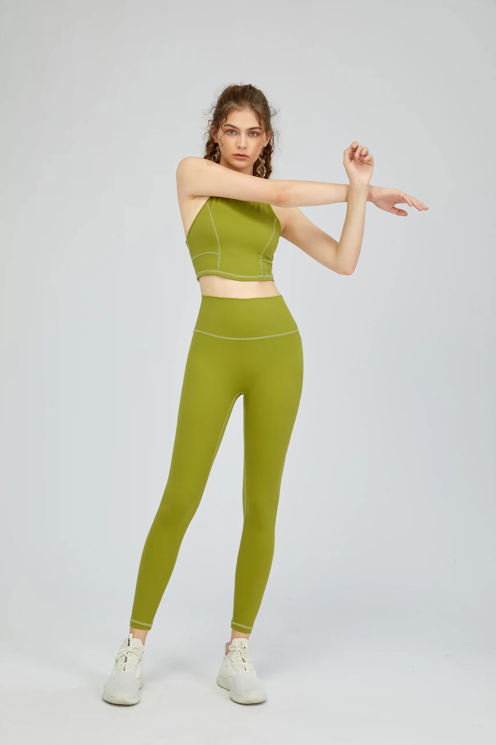 Female model in green yoga set stretching arms, showcasing flexibility and fit.